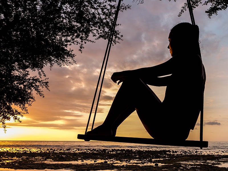 silhouette of a woman sitting on a swing looking at the sun set